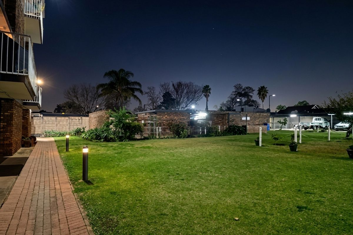 Night view of a communal garden area featuring a brick paved walkway, manicured lawn, and perimeter boundary walls with integrated bollard lighting.