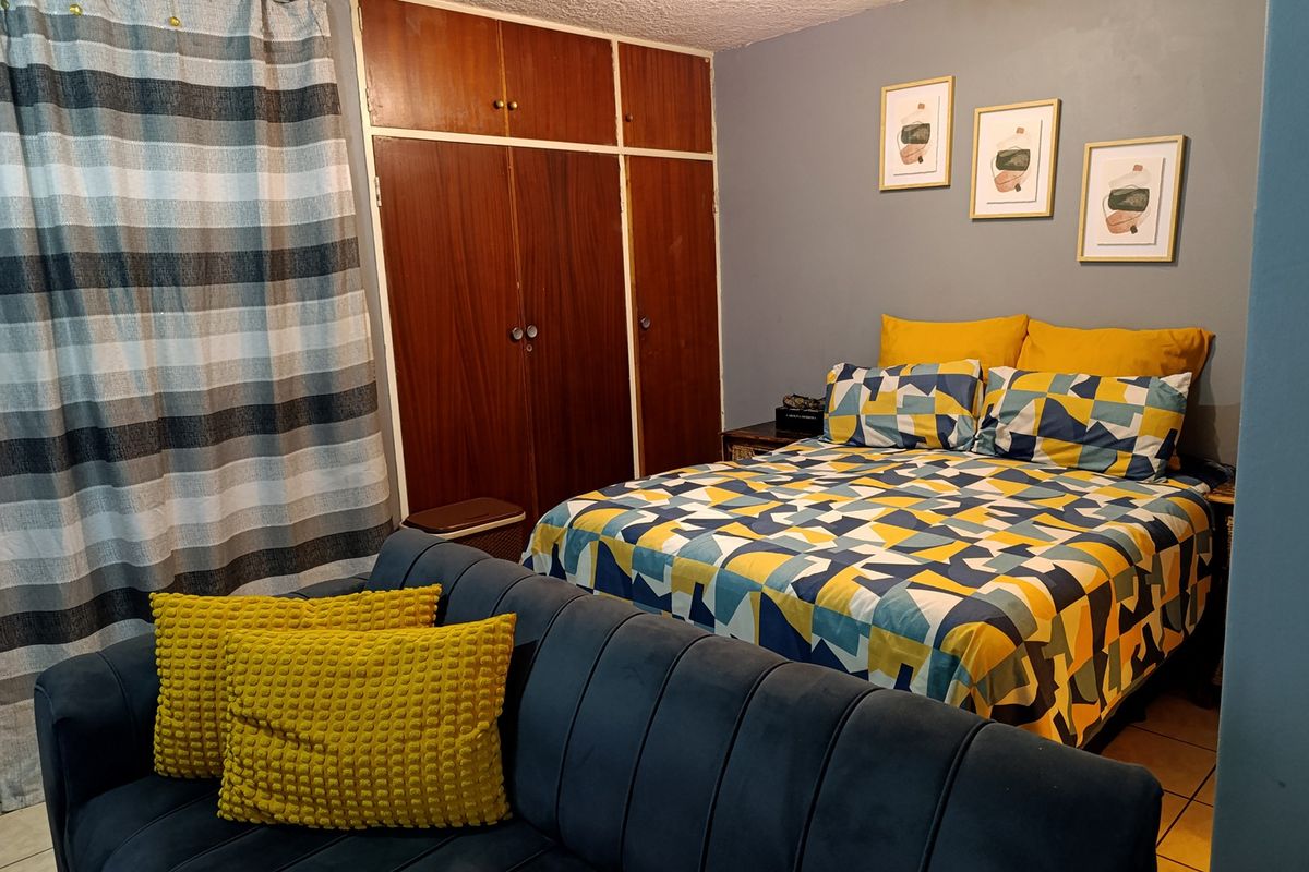A bedroom featuring built-in wooden wardrobes, tiled flooring, and a textured ceiling, offering a functional space with potential for modern updates.