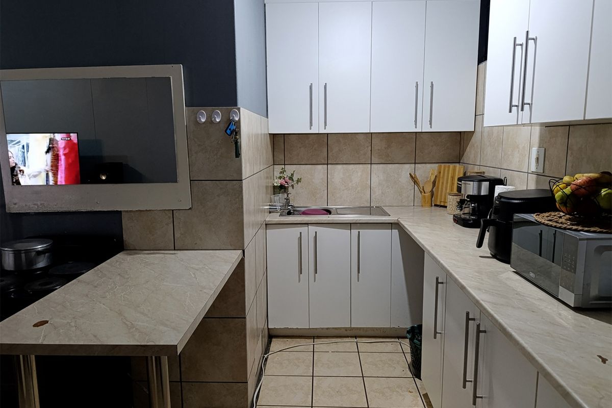 A functional kitchen featuring white built-in cabinetry, laminate countertops, stainless steel sink, and neutral ceramic wall and floor tiling.