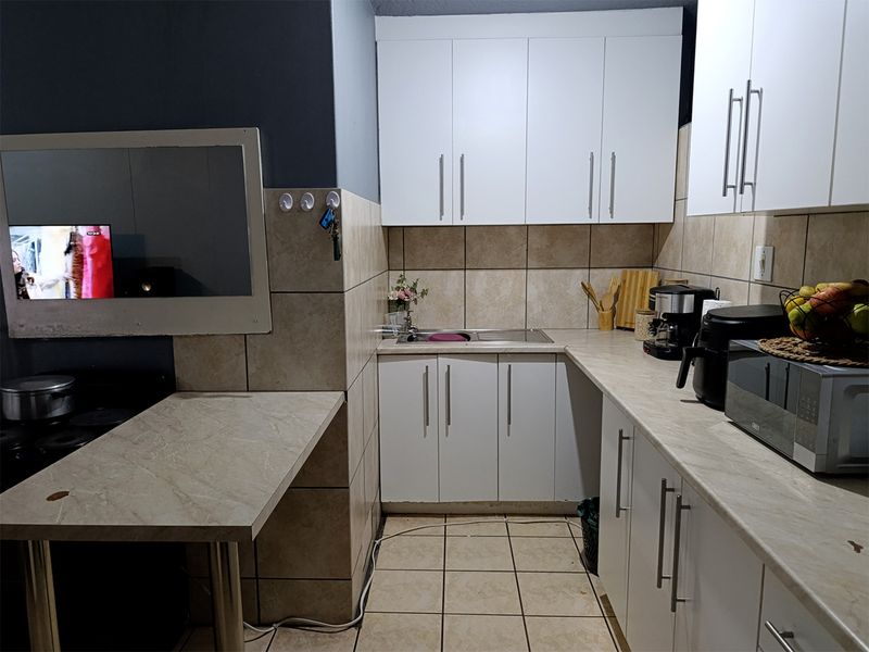 A functional kitchen featuring white built-in cabinetry, laminate countertops, stainless steel sink, and neutral ceramic wall and floor tiling.