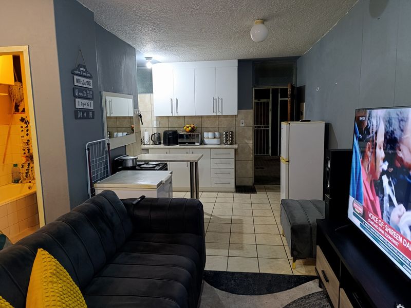 Open-plan living area featuring a compact kitchen with white cabinetry, tiled flooring, and a connected living space.