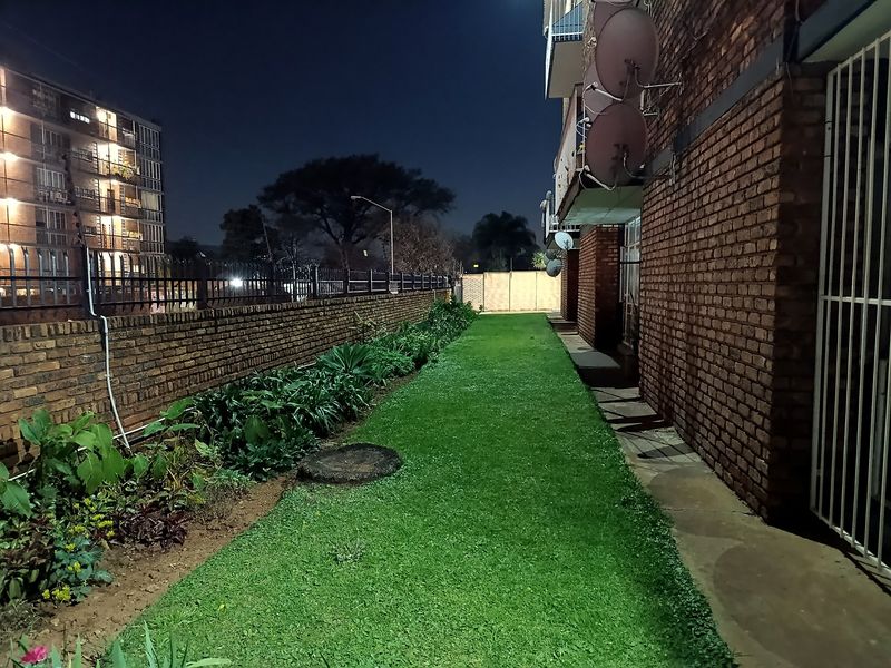 Night view of the apartment building's rear exterior, featuring a brick facade, a narrow lawn area, and a brick boundary wall.