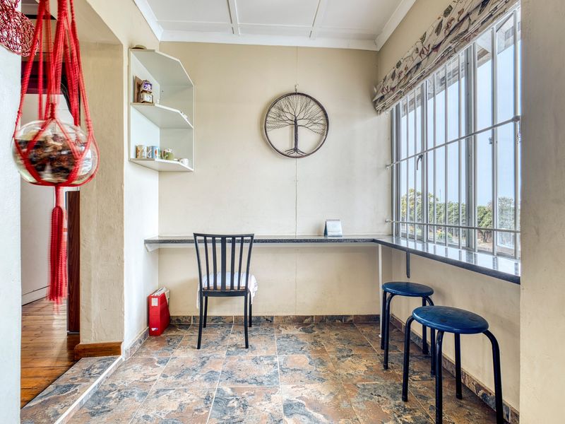 A functional home office space featuring a built-in desk, tiled flooring, and large windows with security bars, offering a practical workspace.