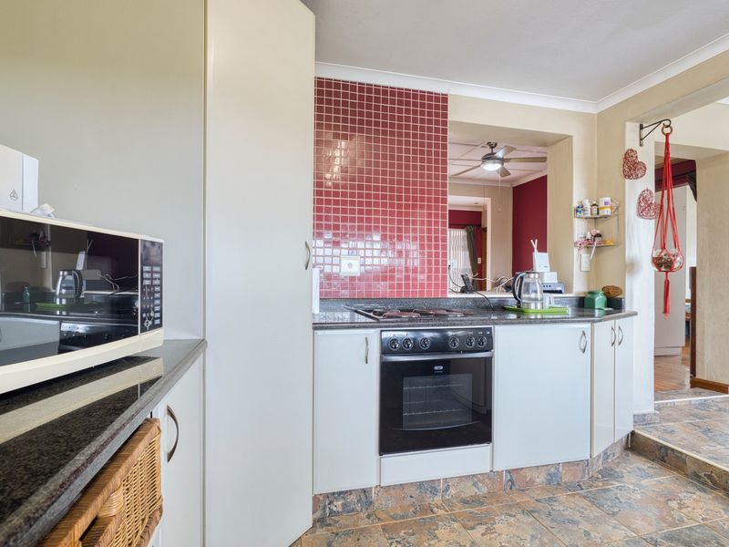 A functional kitchen featuring built-in cabinetry, granite countertops, a hob, an oven, and a distinctive red tiled splashback with tiled flooring.