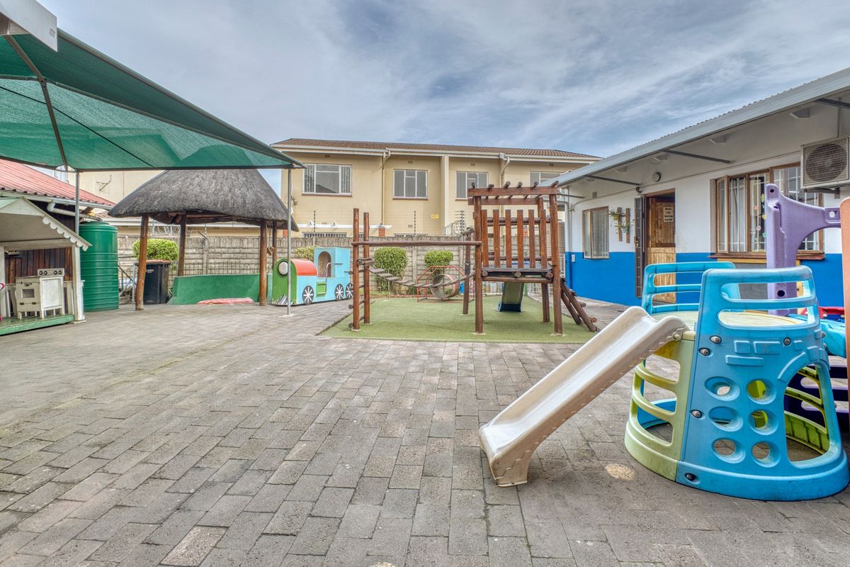 A paved rear courtyard featuring a shade sail, a thatch gazebo, and a water tank, currently utilized as an outdoor play area.