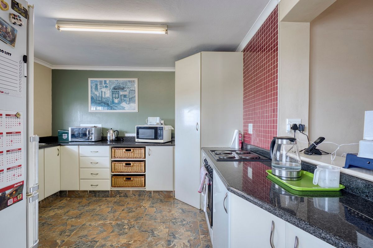 A functional kitchen featuring white cabinetry, dark granite countertops, a red tiled splashback, and durable tiled flooring with integrated cooking appliances.