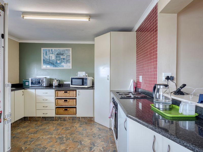 A functional kitchen featuring white cabinetry, dark granite countertops, a red tiled splashback, and durable tiled flooring with integrated cooking appliances.