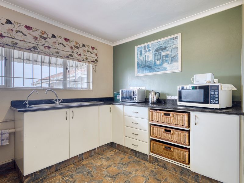 A functional kitchen featuring white cabinetry, dark granite countertops, a double sink, and tiled flooring with a green accent wall.