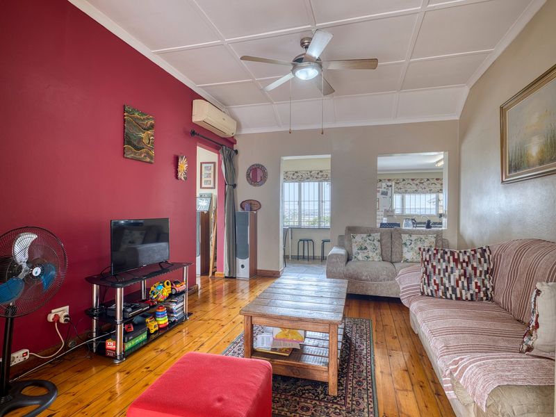 Living room featuring timber flooring, a ceiling fan, split-system air conditioning, and a pass-through window connecting to the kitchen area.