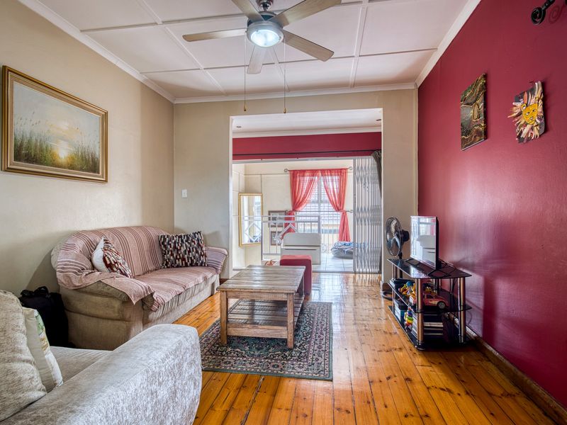 A living room featuring polished hardwood flooring, a ceiling fan, and an open transition to an adjacent balcony area with security gate access.
