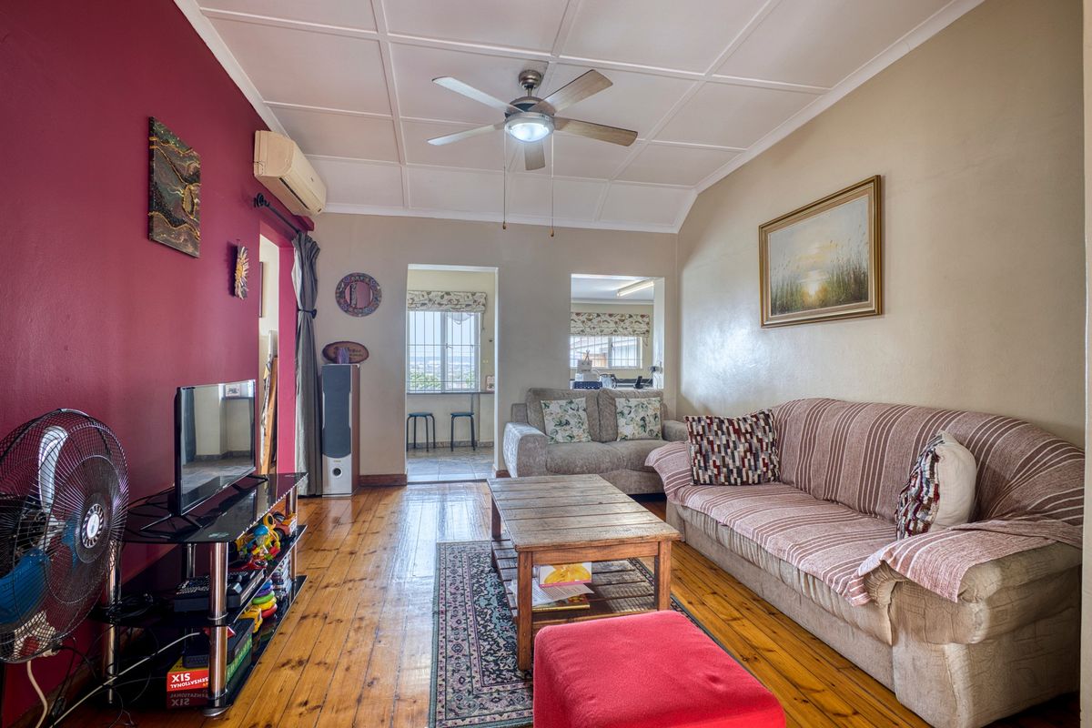 A living room featuring timber flooring, a ceiling fan, and a split-system air conditioner, with access to an adjoining space.