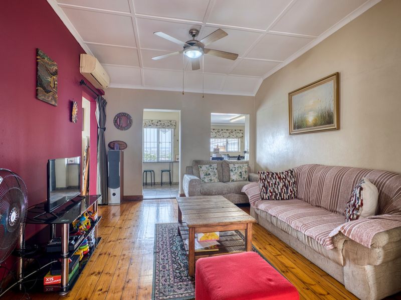 A living room featuring timber flooring, a ceiling fan, and a split-system air conditioner, with access to an adjoining space.