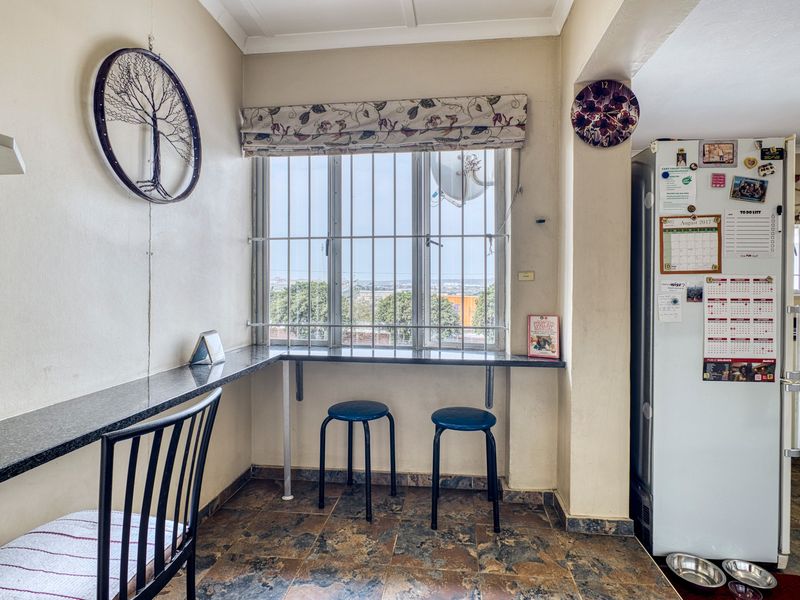 A functional kitchen area featuring a granite breakfast counter, tiled flooring, and security bars on the window overlooking the exterior.