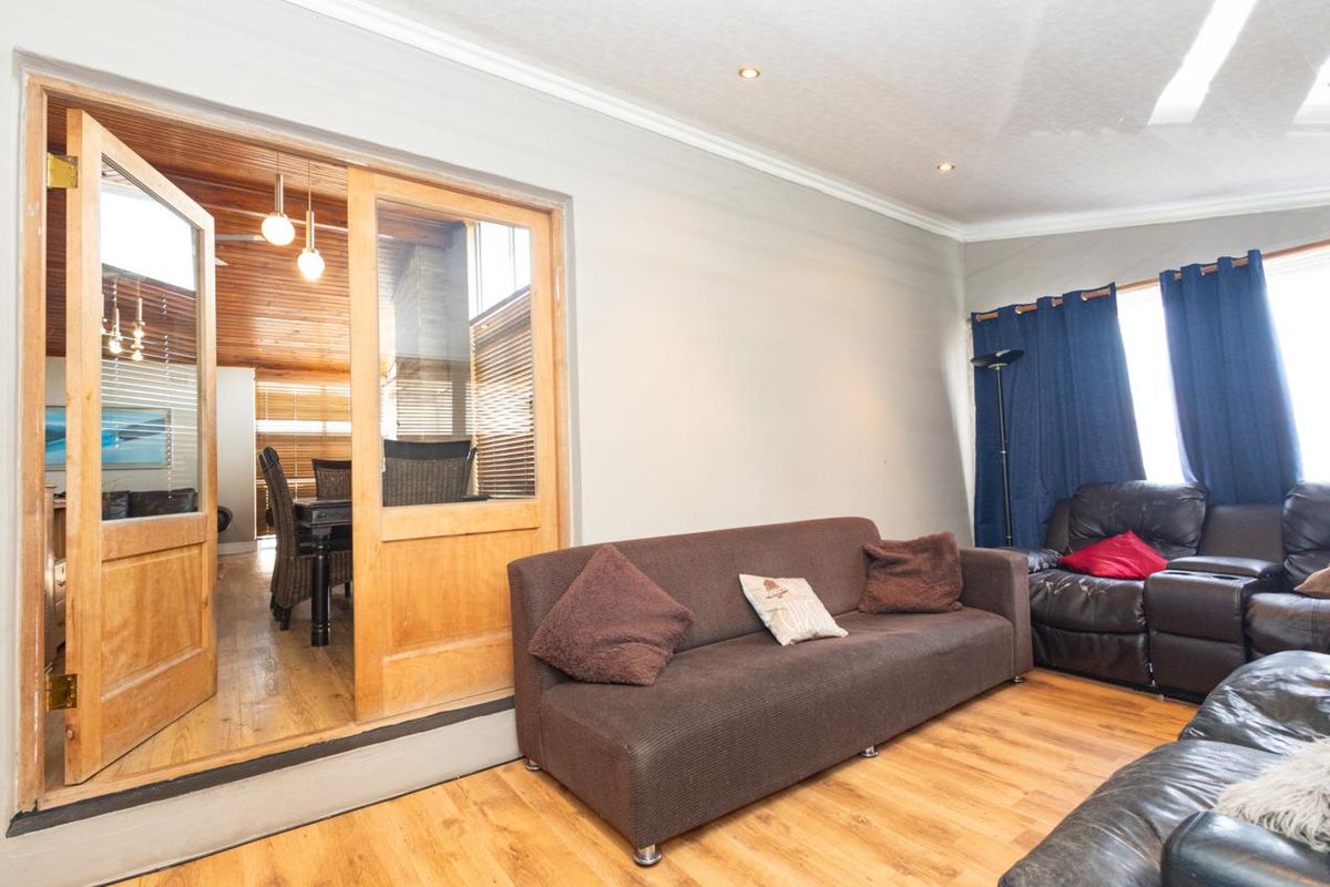 A living room featuring laminate flooring, recessed downlights, and timber-framed glass double doors leading to an adjacent space.