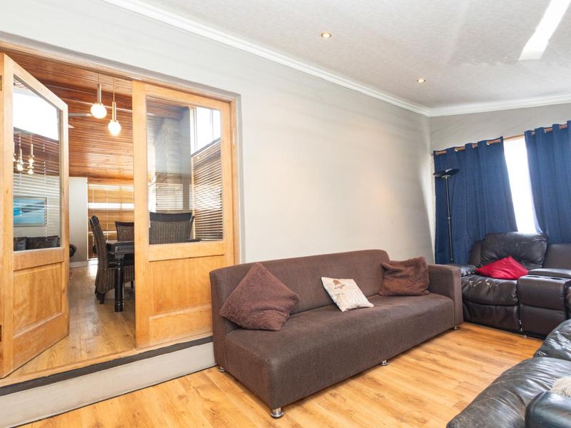 A living room featuring laminate flooring, recessed downlights, and timber-framed glass double doors leading to an adjacent space.