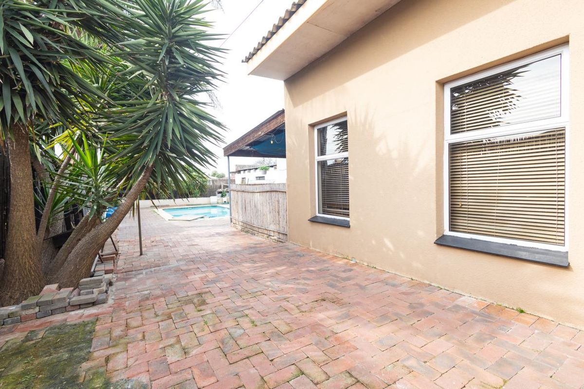 Rear exterior view featuring a paved patio area, swimming pool, and building facade with aluminium windows.