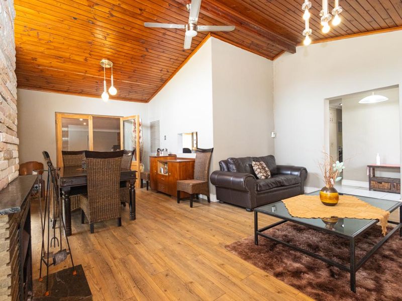 Spacious open-plan living and dining area featuring a striking timber-clad vaulted ceiling, stone fireplace, and warm laminate flooring.
