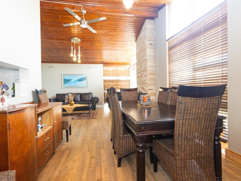 Spacious open-plan living and dining area featuring a vaulted timber ceiling, stone feature wall, and large windows with venetian blinds.