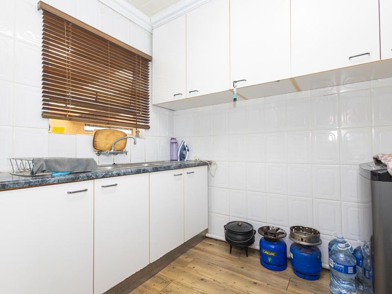 Functional laundry area featuring white built-in cabinetry, laminate countertops, stainless steel sink, and tiled splashbacks with durable laminate flooring.
