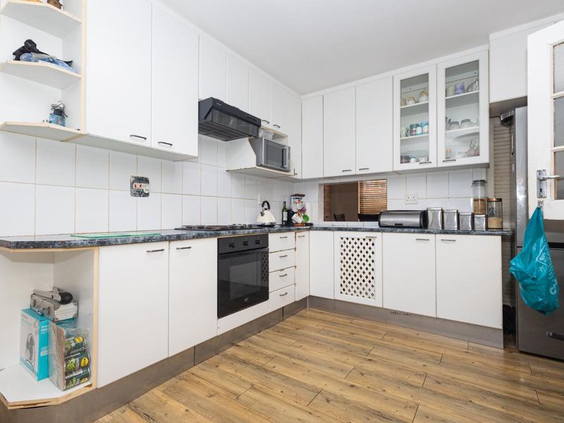 A functional kitchen featuring white cabinetry, laminate countertops, built-in oven, extractor fan, and wood-look laminate flooring with a tiled backsplash.