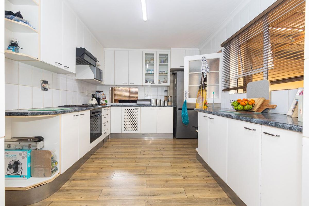 A functional kitchen featuring white cabinetry, laminate countertops, built-in oven, hob, and extractor fan with wood-look flooring and tiled backsplash.