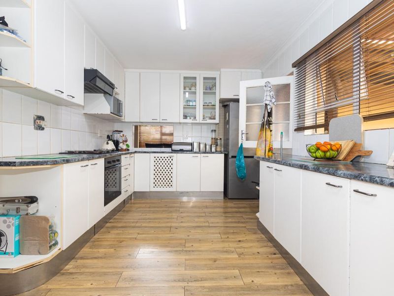 A functional kitchen featuring white cabinetry, laminate countertops, built-in oven, hob, and extractor fan with wood-look flooring and tiled backsplash.