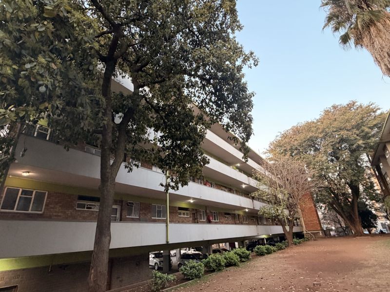 Exterior view of a multi-story apartment building featuring brick facade, concrete walkways, and an integrated ground-level covered parking area.