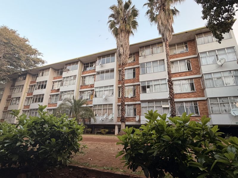 A multi-story residential apartment block featuring a brick facade and large windows, set within a landscaped garden area.