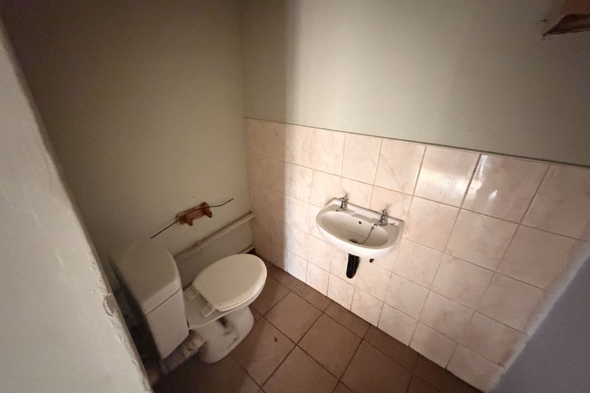 A compact bathroom featuring a wall-mounted basin, toilet, tiled splashback, and tiled flooring, currently in need of cosmetic updates and minor repairs.