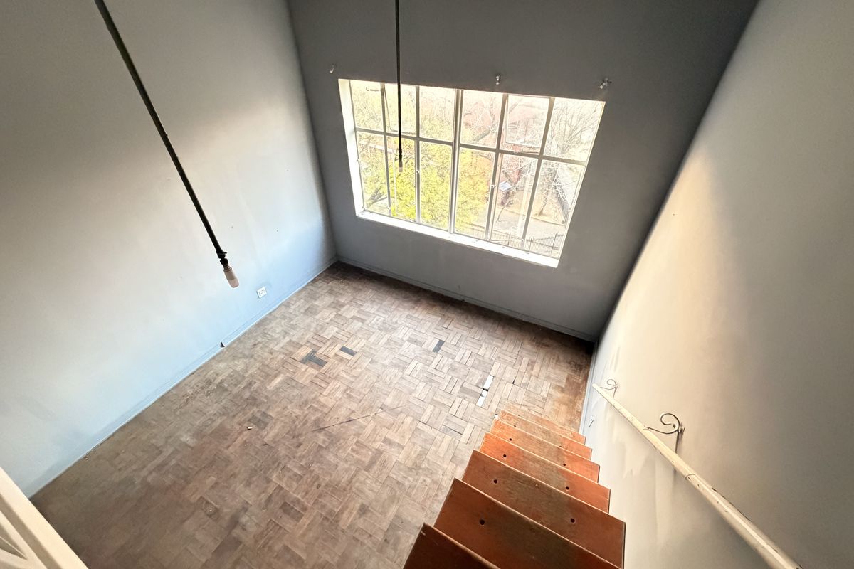 An empty living area featuring original parquet flooring, a large window providing natural light, and a staircase leading to the upper level.