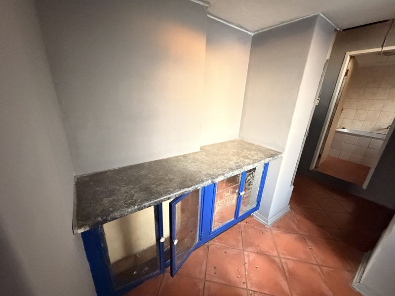 A hallway area featuring built-in blue cabinetry with a laminate countertop and terracotta floor tiles, leading towards a bathroom.