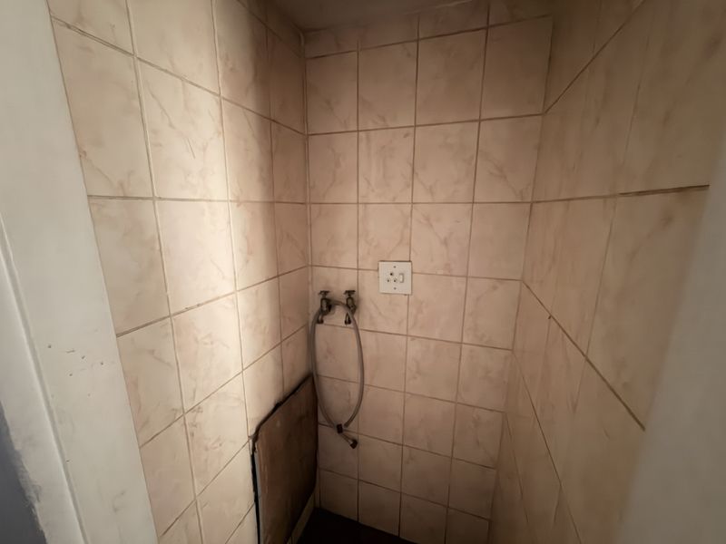 A dedicated laundry alcove featuring tiled walls, plumbing connections for a washing machine, and an electrical outlet.