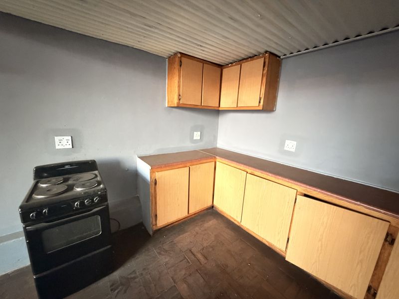 A basic kitchen area featuring wooden cabinetry, laminate countertops, a freestanding stove, and a corrugated metal ceiling finish.