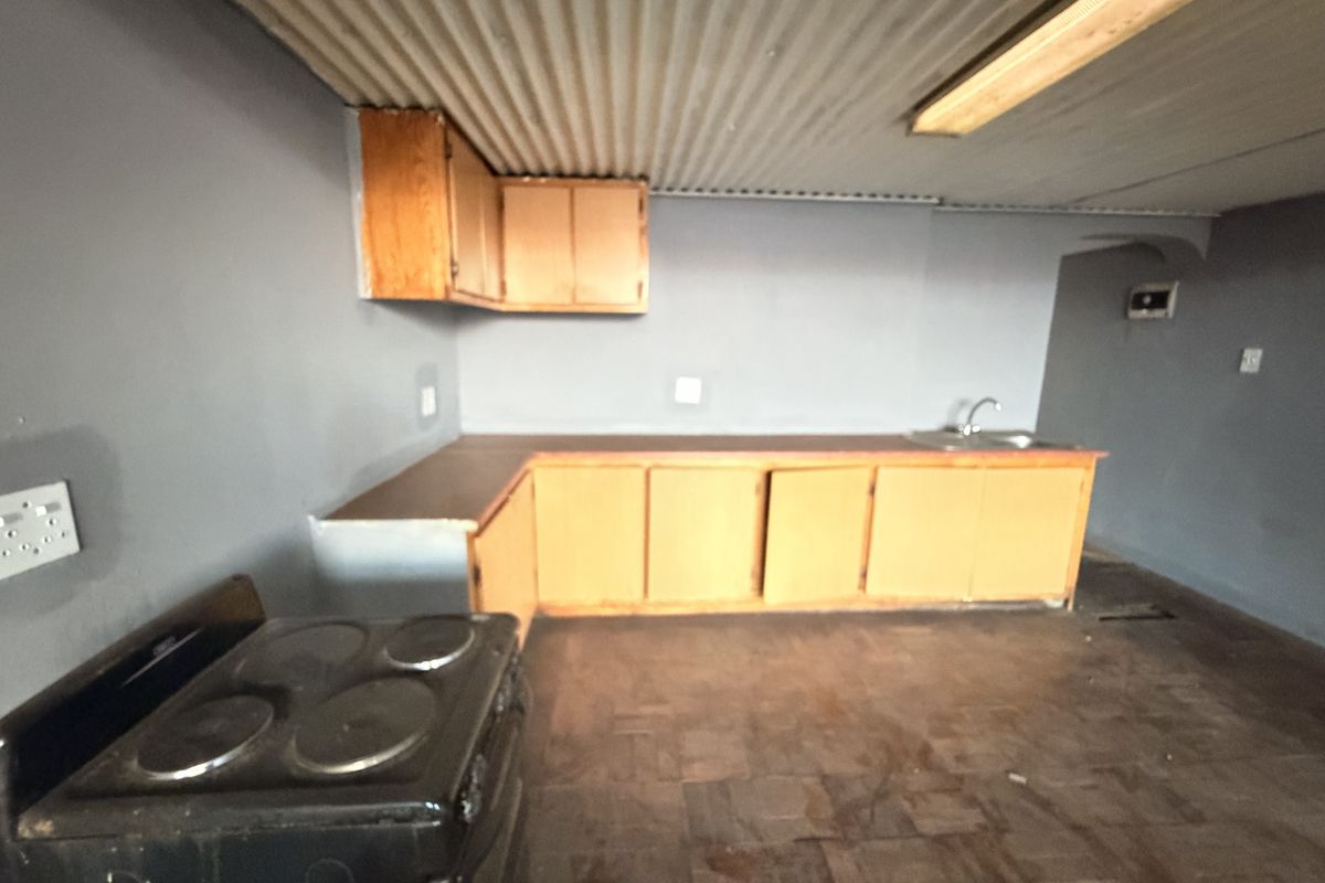 A dated kitchen area featuring built-in wooden cabinetry, a stainless steel sink, and a corrugated metal ceiling, offering potential for modernization.