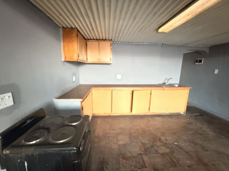 A dated kitchen area featuring built-in wooden cabinetry, a stainless steel sink, and a corrugated metal ceiling, offering potential for modernization.