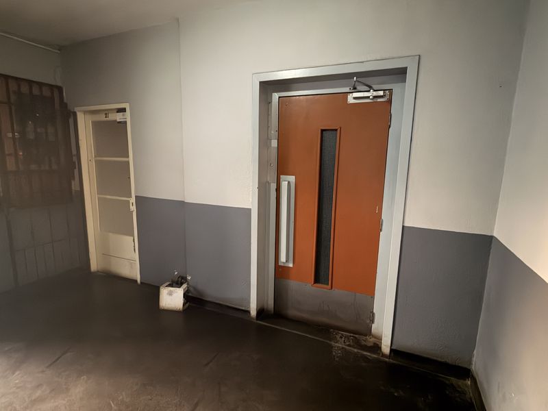 A functional apartment building hallway featuring a fire-rated door, security gate, and painted walls with durable flooring.
