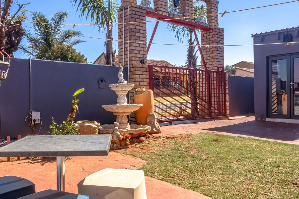 A rear courtyard area featuring a brick boundary wall, decorative gate structure, paved patio space, and a small lawn.