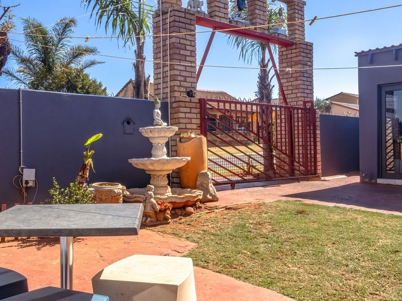 A rear courtyard area featuring a brick boundary wall, decorative gate structure, paved patio space, and a small lawn.