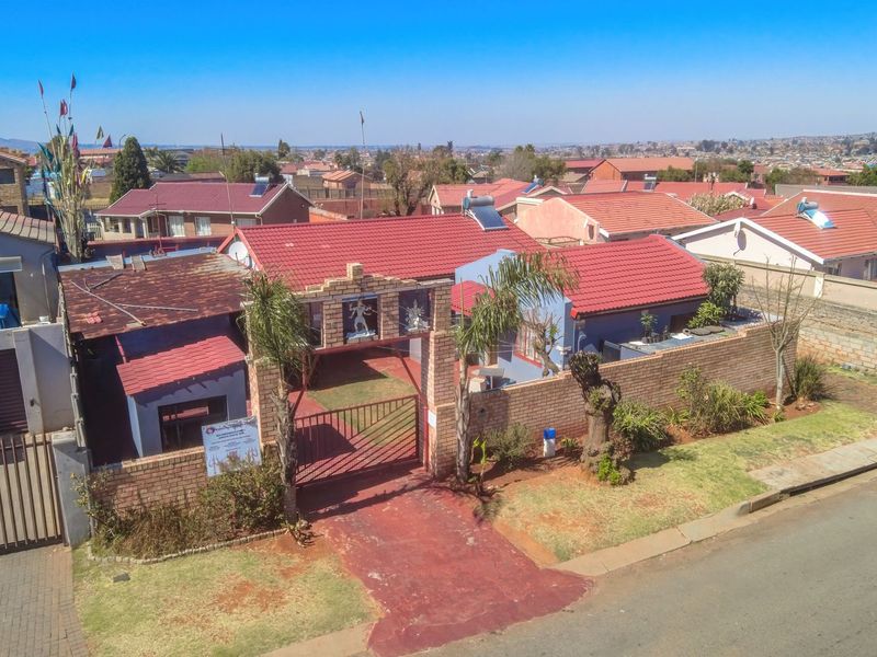 Aerial view of a residential property featuring a tiled roof, brick boundary wall, and gated driveway access in a suburban neighborhood.