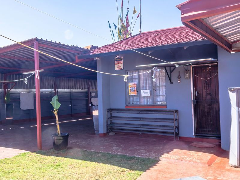 Rear exterior view of the house featuring a covered carport area, tiled roof, and secure entrance with a security gate.