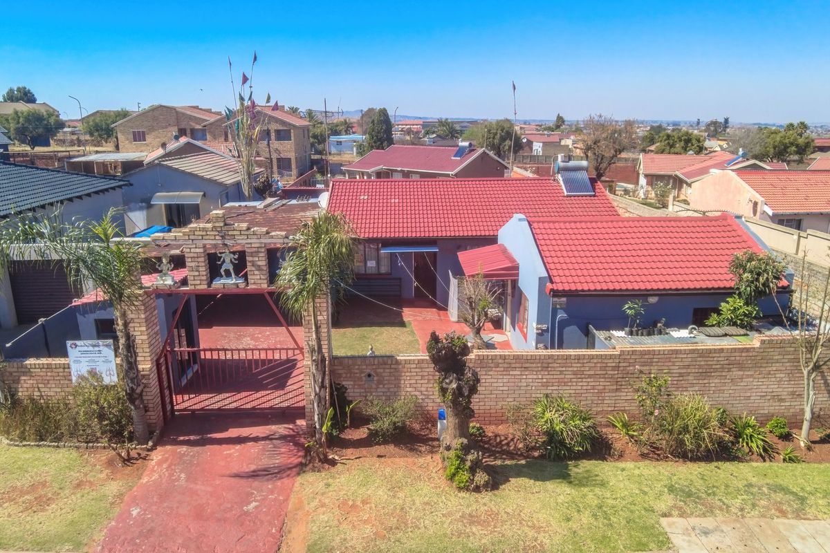 Aerial view of a residential property featuring a brick boundary wall, gated entrance, tiled roof, and solar water heating system.