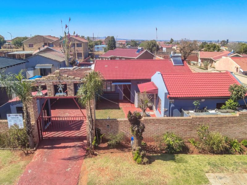 Aerial view of a residential property featuring a brick boundary wall, gated entrance, tiled roof, and solar water heating system.