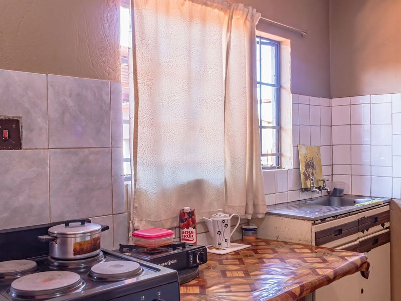 A functional kitchen featuring a built-in stainless steel sink, tiled splashback, and electric stove, requiring cosmetic updates to modernize the space.