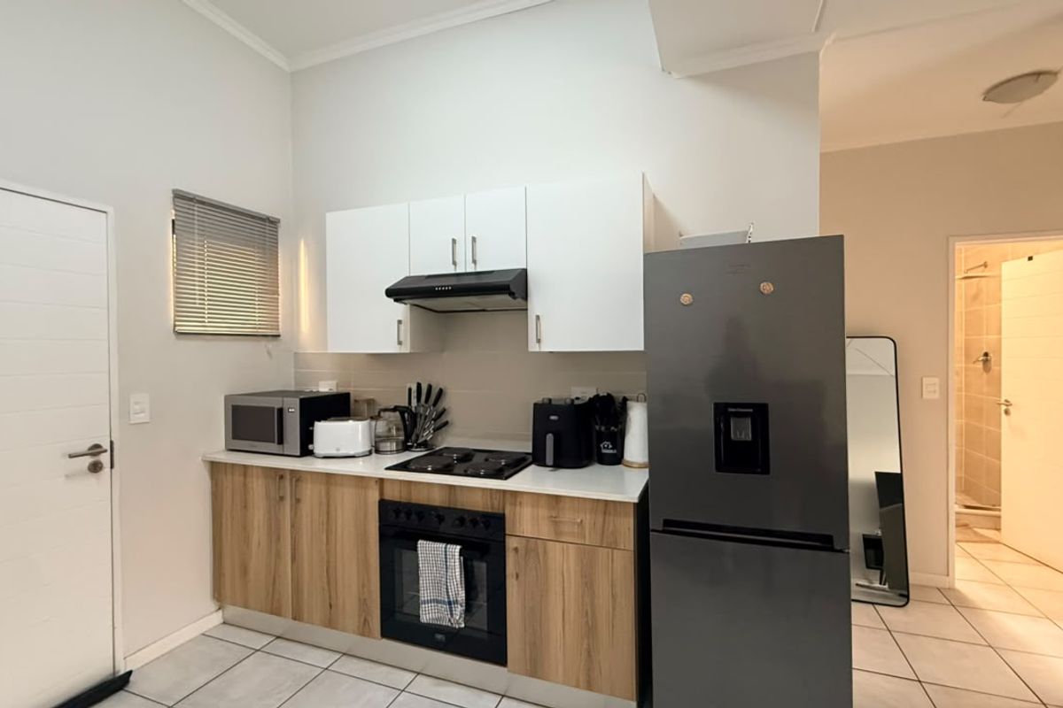 Compact kitchen featuring modern wood-finish lower cabinetry, white upper cabinets, built-in oven and hob, and tiled flooring, with an adjacent bathroom visible.