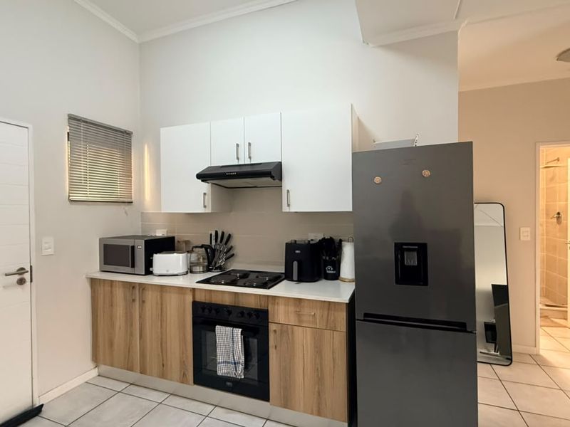 Compact kitchen featuring modern wood-finish lower cabinetry, white upper cabinets, built-in oven and hob, and tiled flooring, with an adjacent bathroom visible.