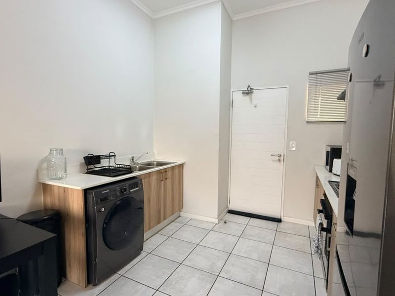 Functional laundry area featuring built-in cabinetry, a stainless steel sink, tiled flooring, and direct access to an external door.