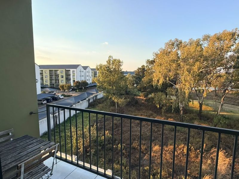 A private balcony featuring a metal balustrade and tiled flooring, offering an elevated view of the surrounding landscape and complex grounds.