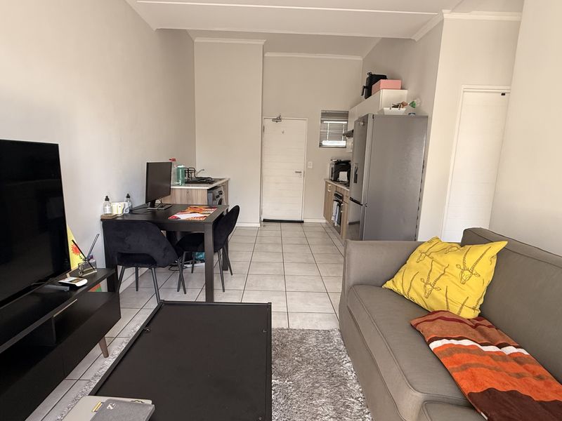 Open-plan living area featuring tiled flooring and a compact kitchen with built-in cabinetry, stove, and extractor fan.