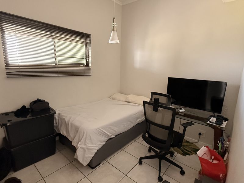 A compact bedroom featuring tiled flooring, a window with venetian blinds, and a central pendant light fixture.