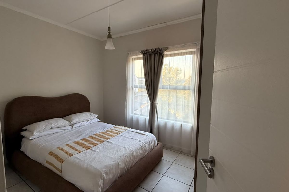 A well-lit bedroom featuring neutral wall tones, tiled flooring, and a large window with curtain tracks, offering a comfortable and functional living space.